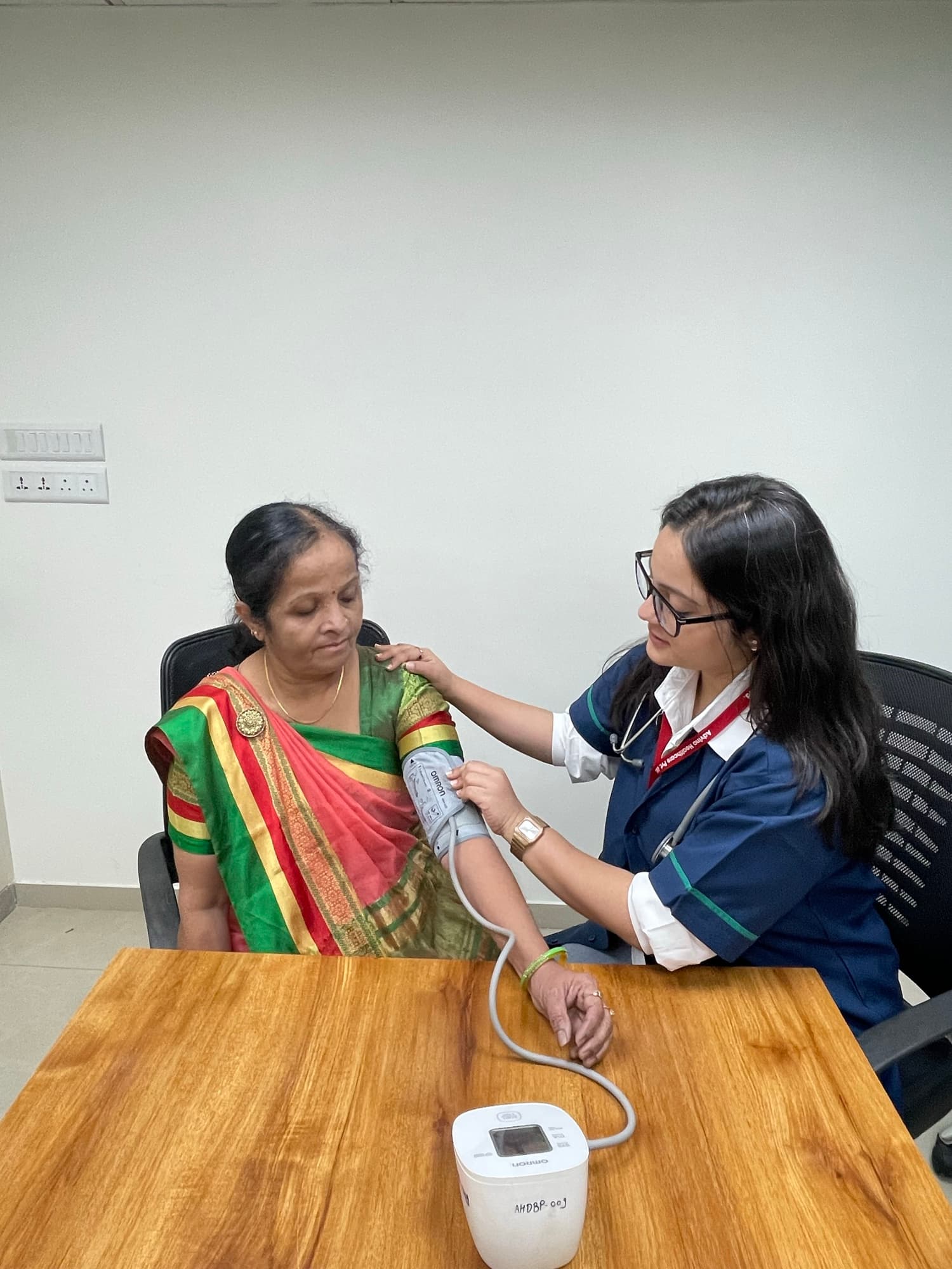 An Advino nurse in uniform checking an elderly woman's blood pressure with a digital monitor.