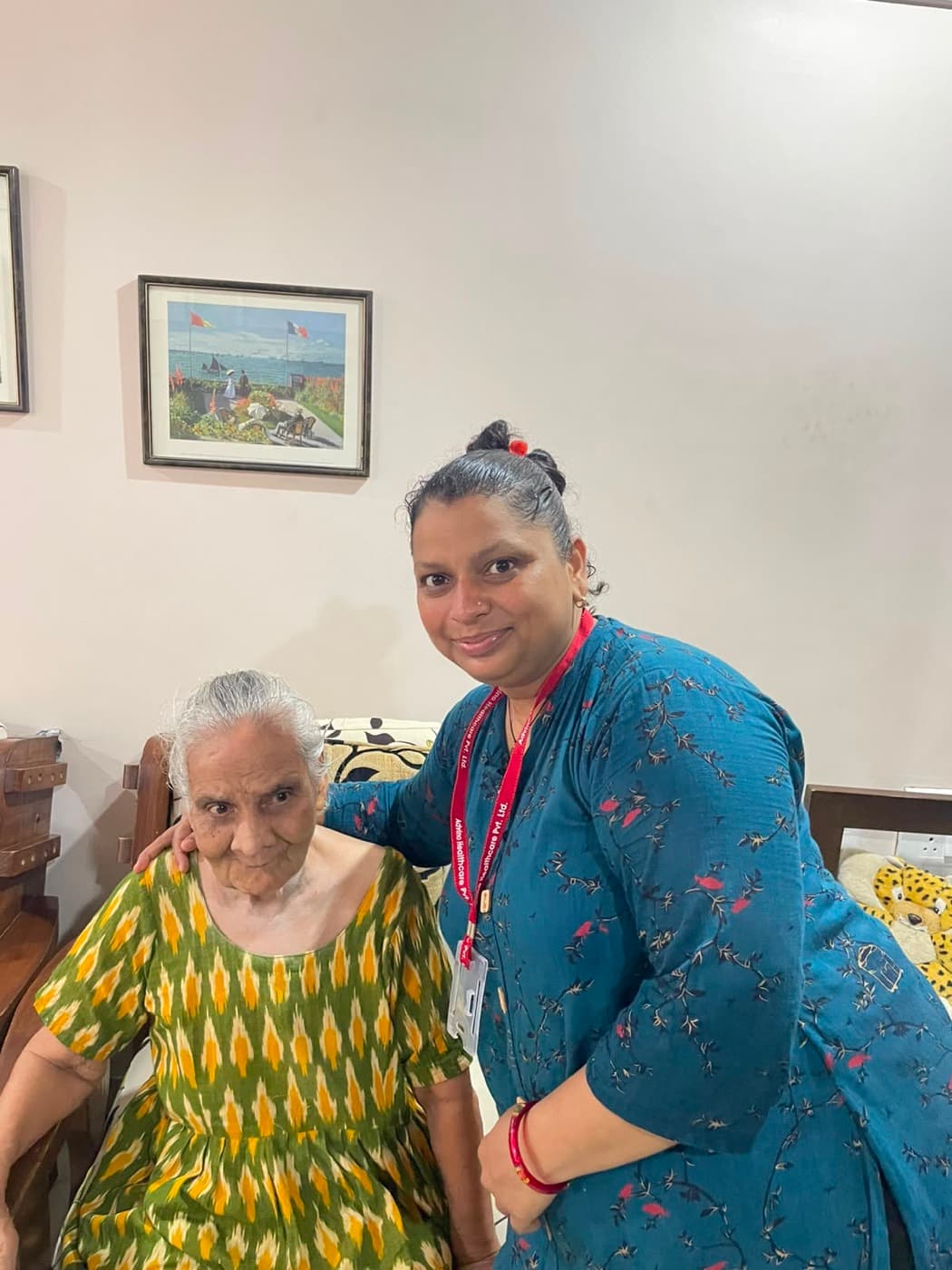 An Advino caregiver standing with an elderly woman seated in her living room.