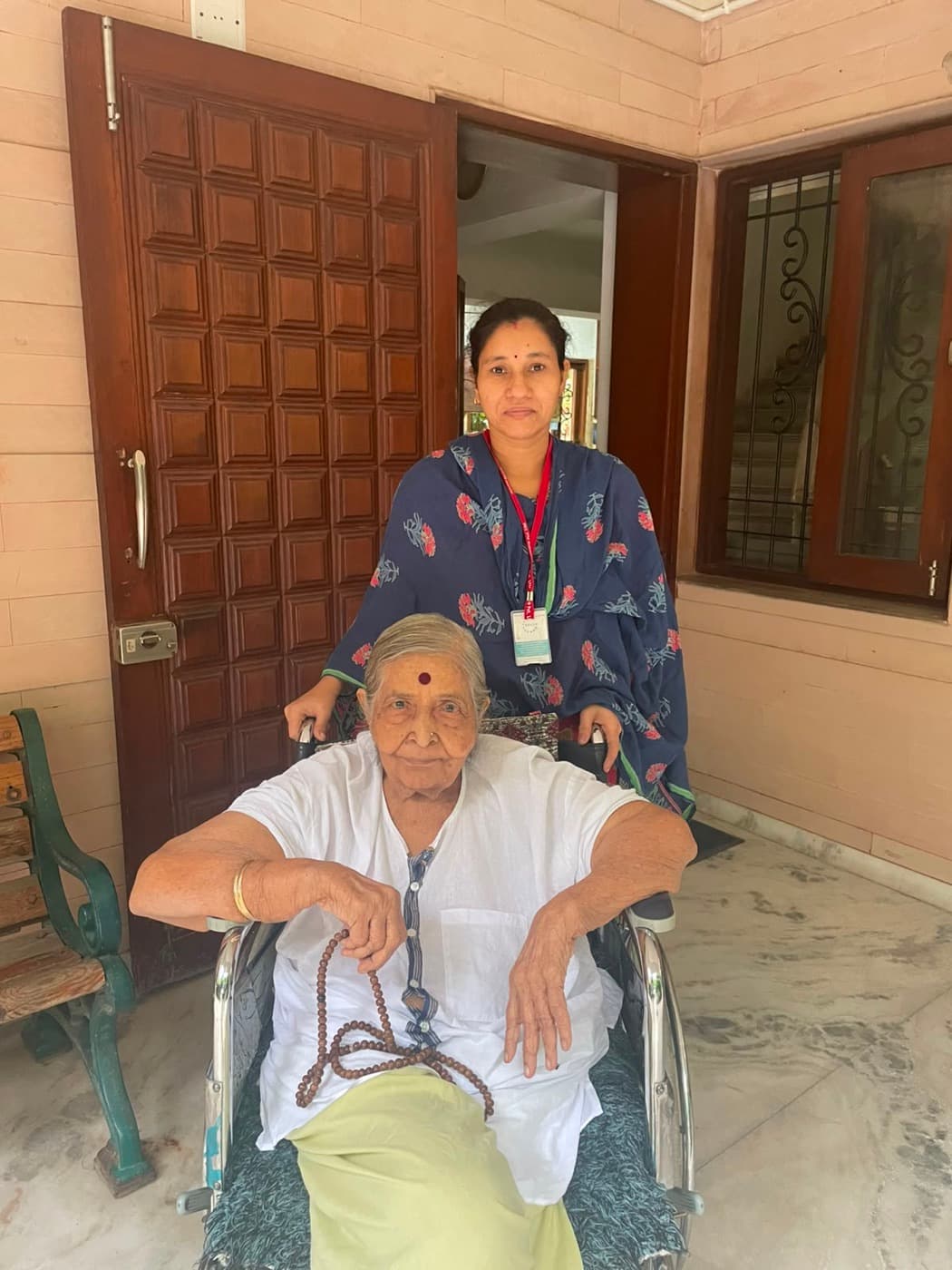 An Advino caregiver with an elderly woman in a wheelchair in the doorway of her home.
